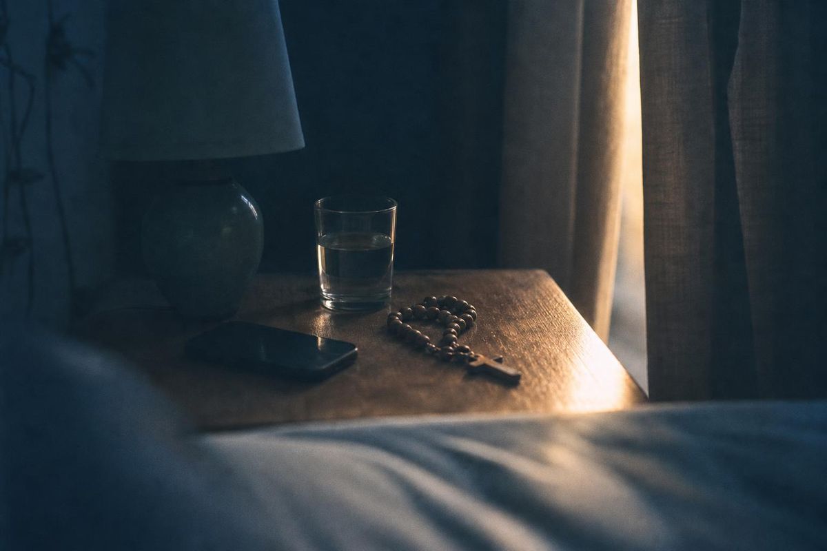 Criado-mudo antes do amanhecer, com o celular virado para baixo e um terço